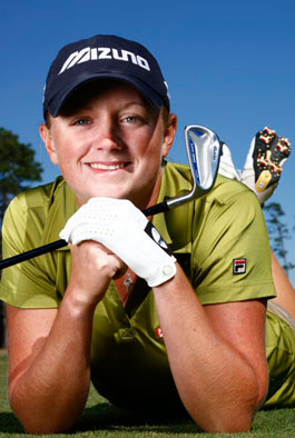 Female golfer posing for photo with golf club in hand on the ground